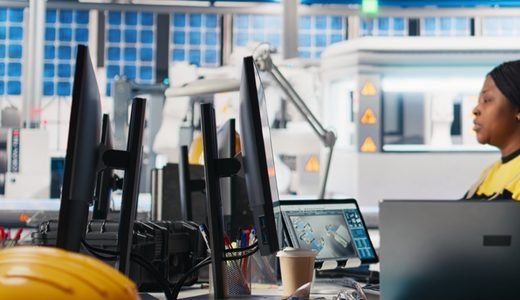 Une ingénieure devant des écrans de conception, casque de chantier posé sur le bureau