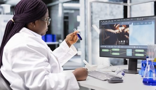 Une chercheuse en blouse blanche observe un échantillon devant un écran d'analyse